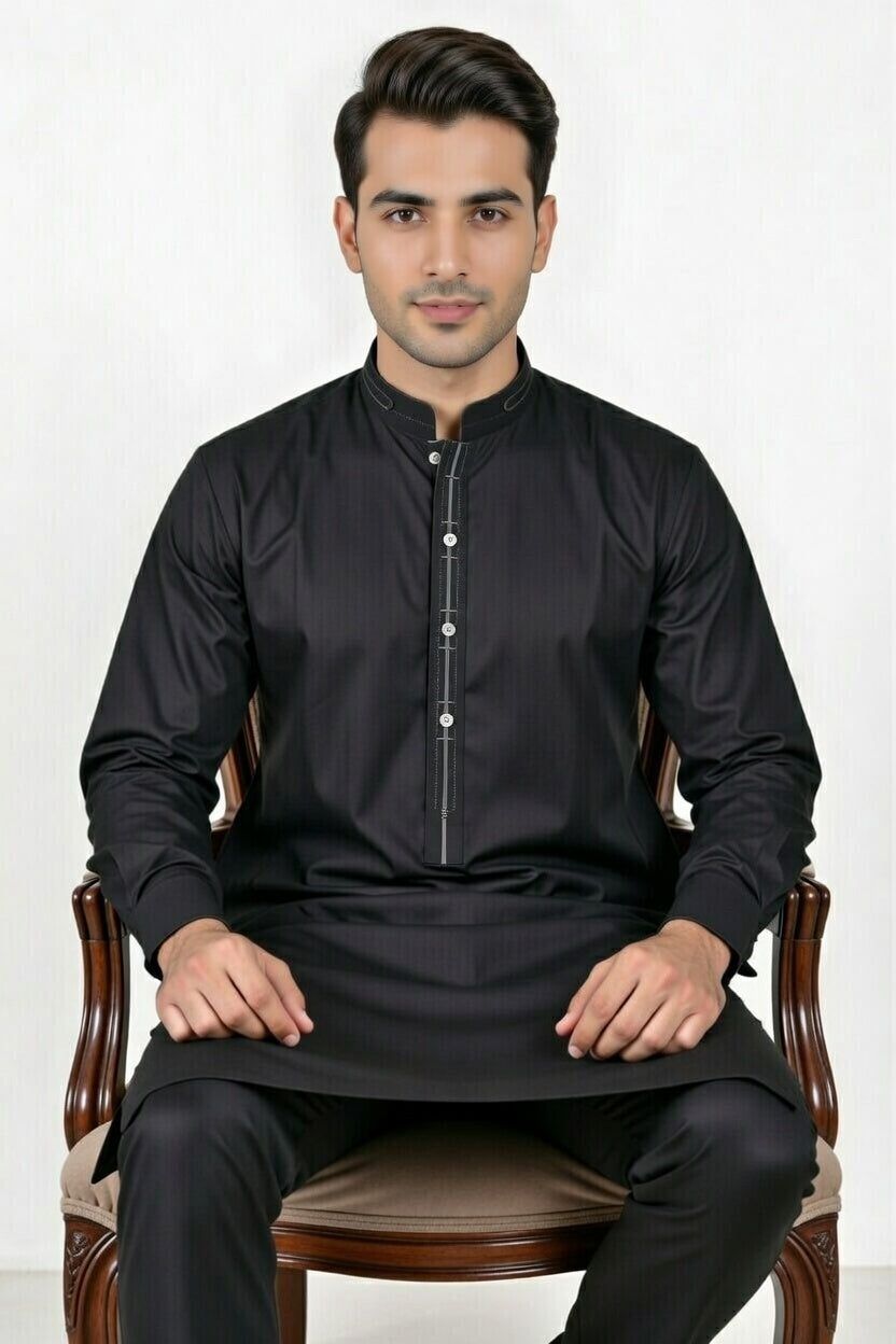 Man wearing a black traditional outfit sitting on a chair against a white background