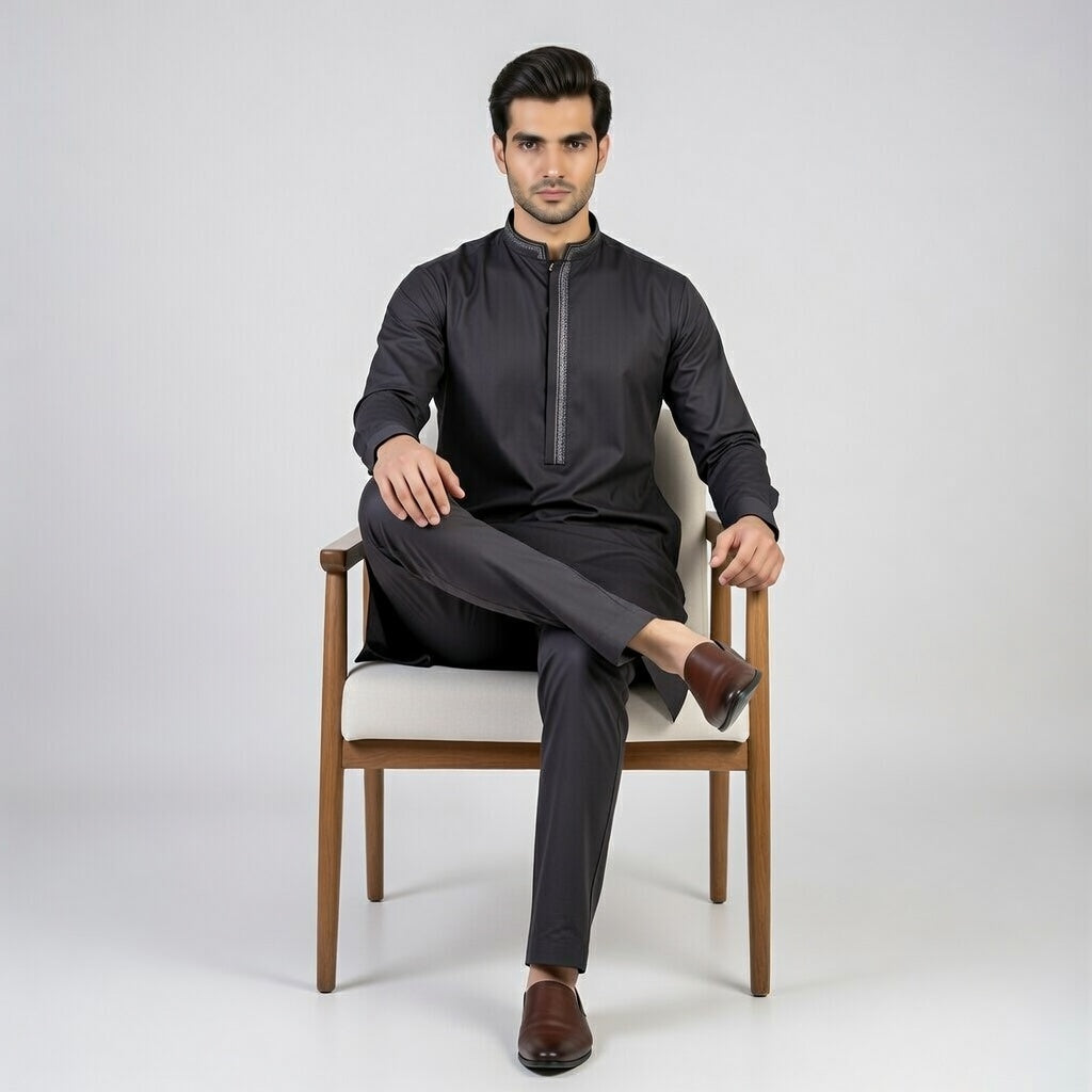 Man sitting on a chair wearing a black outfit against a white background