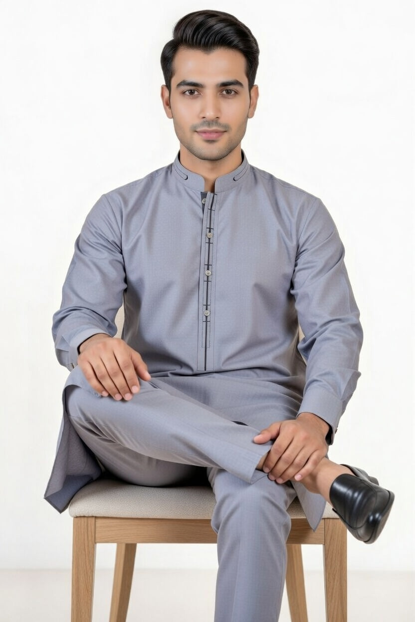 Man wearing a gray traditional outfit sitting on a chair with a white background