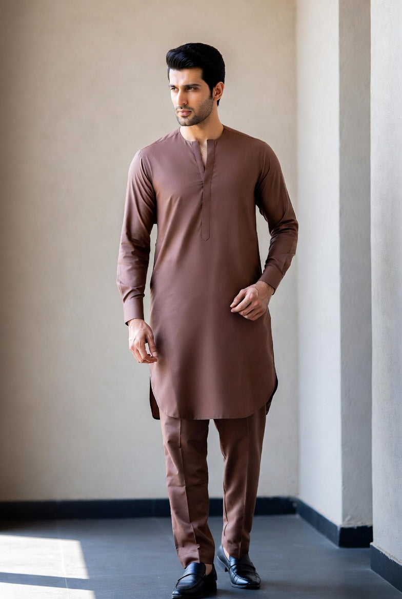Man wearing a brown kurta with pants standing against a neutral wall.