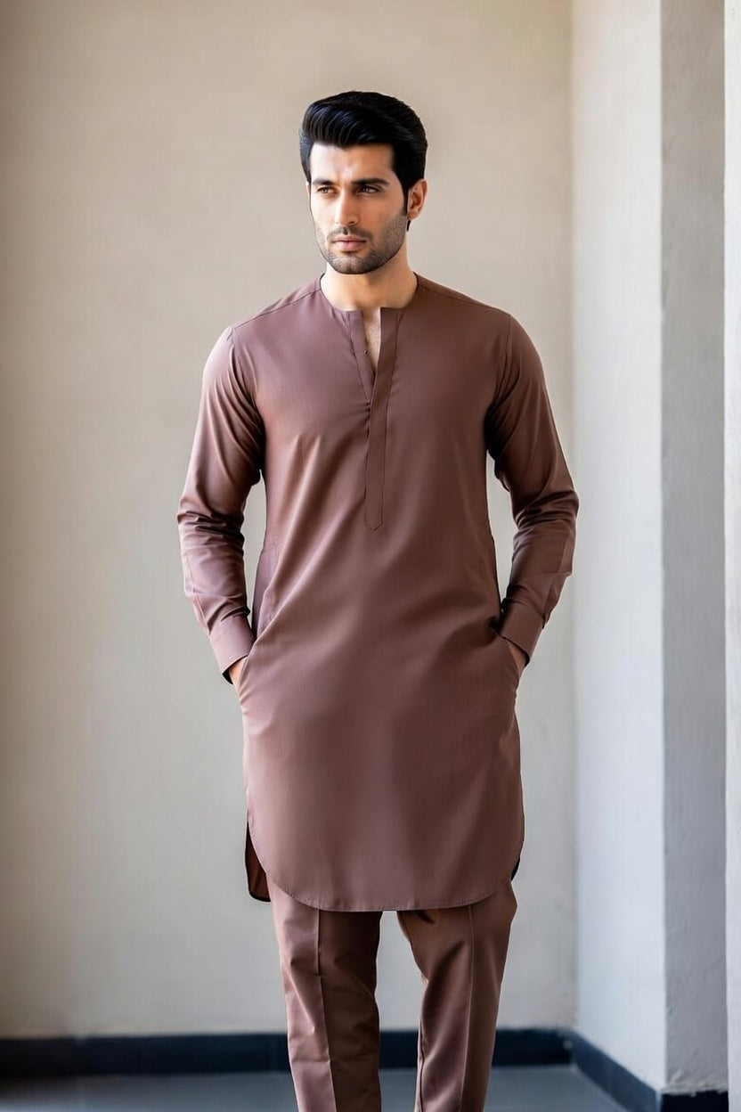 Man wearing a brown kurta standing against a plain wall.
