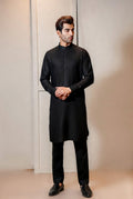 Man wearing a black kurta with black shoes against a neutral background