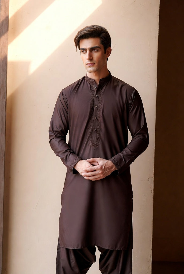 Man wearing a dark brown kurta with pants against a neutral wall.
