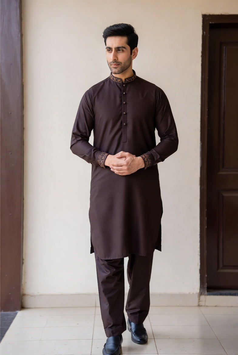 Man wearing a dark brown kurta with pants standing against a plain wall.