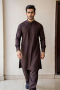 Man wearing a dark brown kurta with pants against a plain wall.