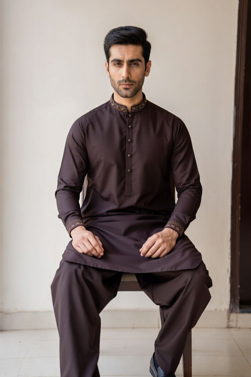 Man wearing a dark brown traditional outfit sitting on a chair.