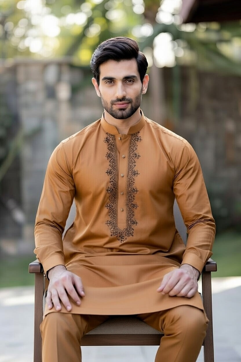 Man wearing a brown kurta with intricate designs, sitting outdoors.
